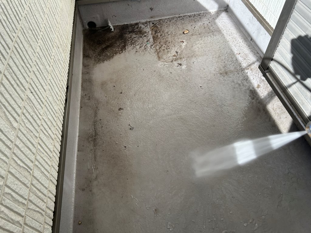 ベランダ床の高圧洗浄作業。トップコート施工前に汚れを除去している様子