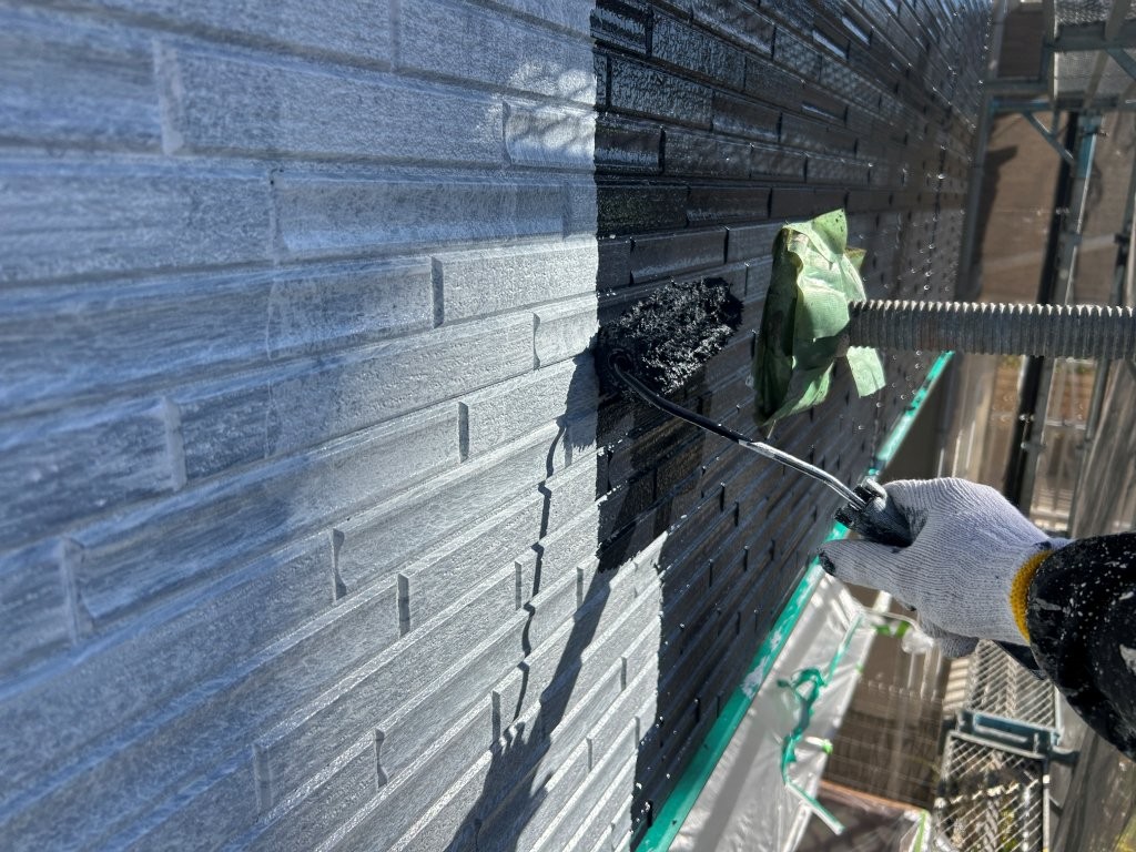 外壁中塗り作業の様子。八潮市S様邸でダークグレー系塗料を塗布している工程